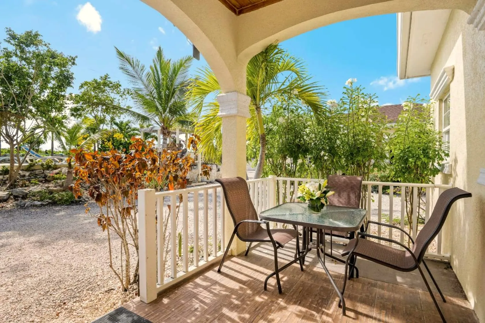 Covered front porch with glass-top dining set and fresh flowers, looking out to palms and the pool area