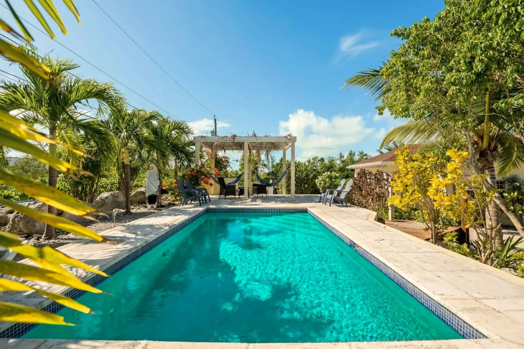 Turquoise pool framed by palm fronds, with a pergola shading twin hammocks and chairs on the stone deck