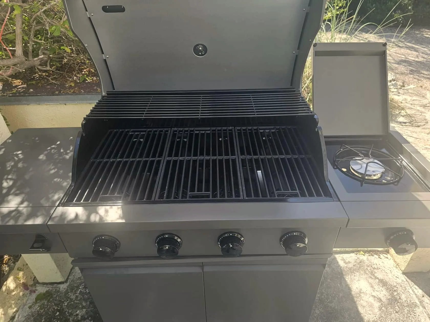 Four-burner gas grill with the lid open, showing clean grates and a side burner