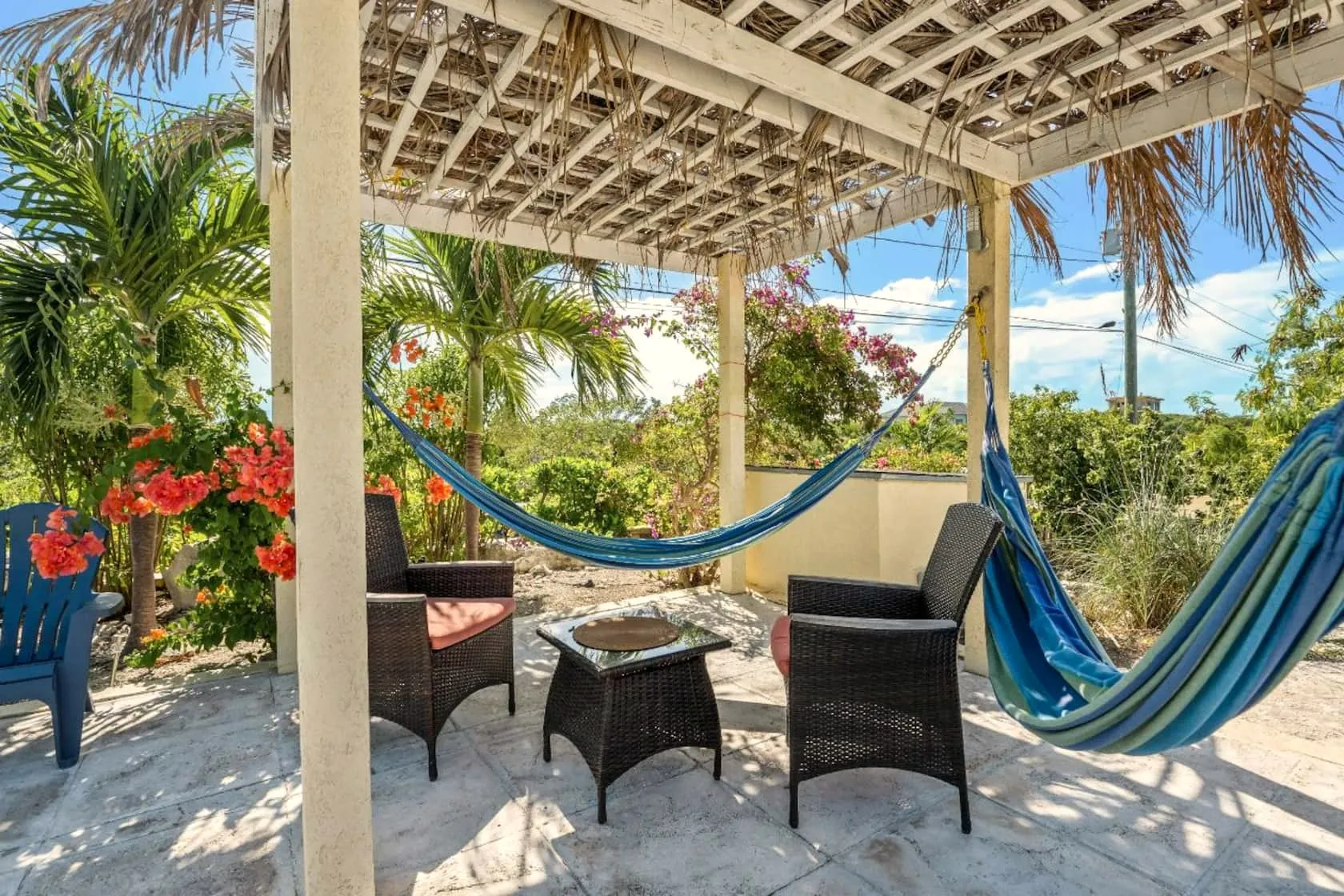 Thatched pergola lounge with twin blue hammocks, wicker chairs, and vivid orange bougainvillea