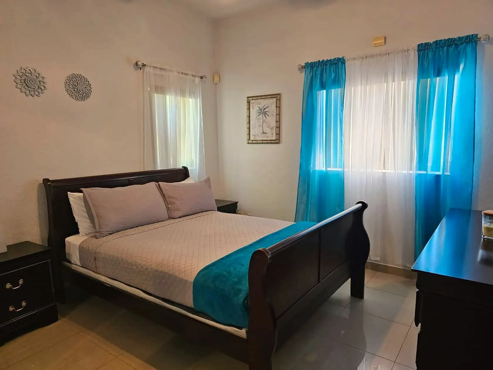 Sea Villa queen bedroom with dark-wood sleigh bed, teal accent throw, and turquoise sheers