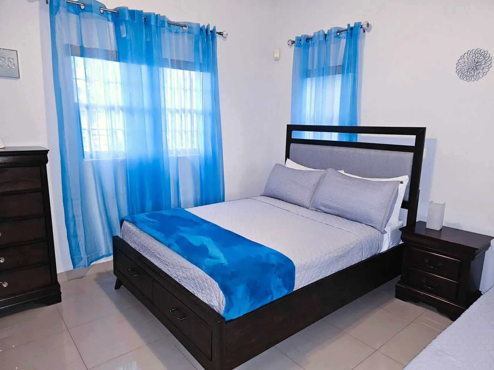 Queen bed with upholstered headboard, under-bed storage drawers, and bright blue sheer curtains