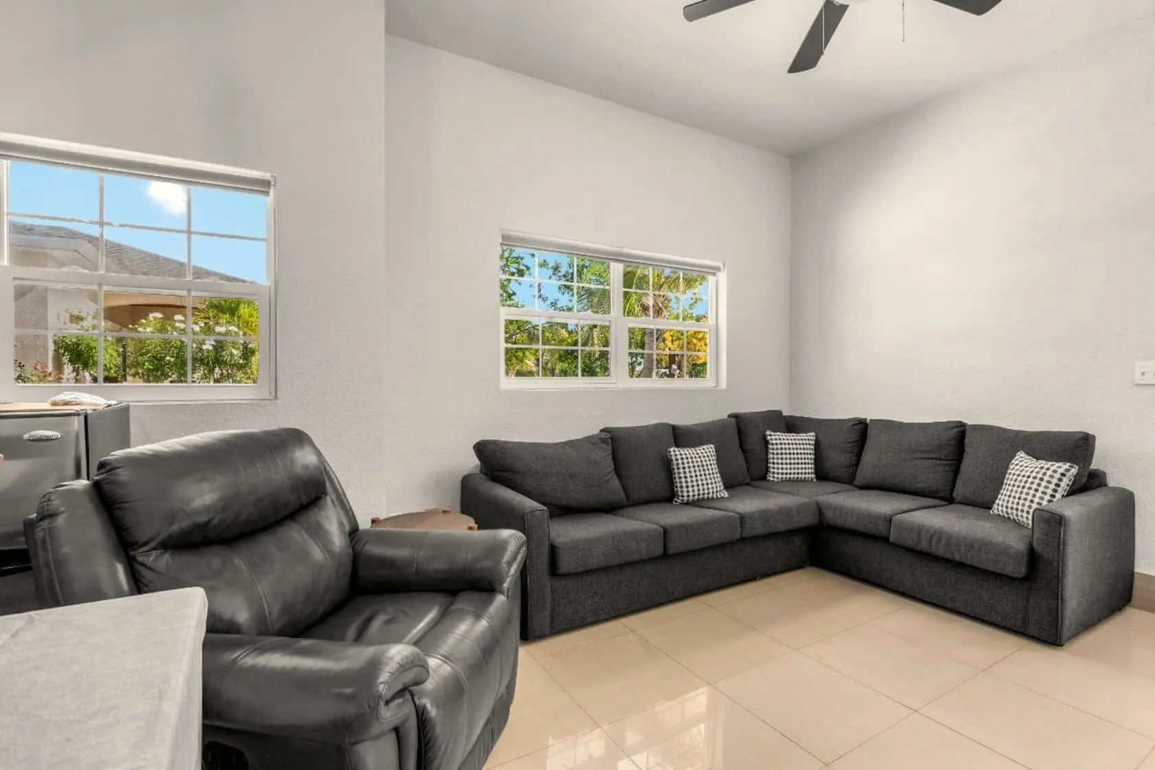 Bright Sun Villa living room with grey sectional, leather recliner, ceiling fan, and garden-view windows