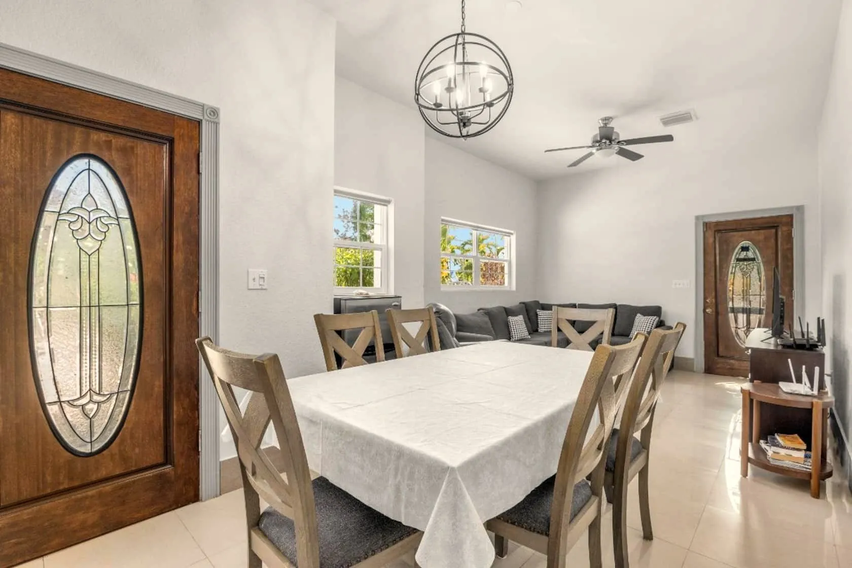 Open dining area with a six-seat farmhouse table, orb chandelier, and leaded-glass entry doors