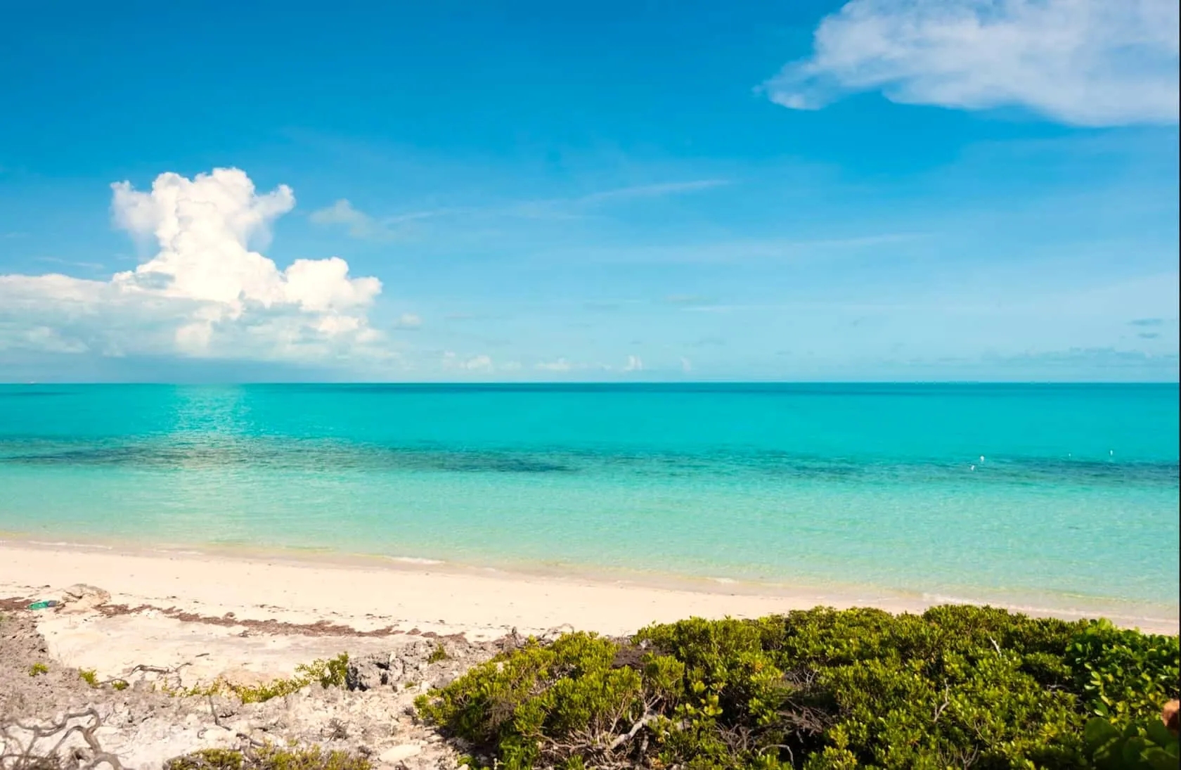 Empty stretch of Long Bay Beach with layered turquoise water under a blue sky